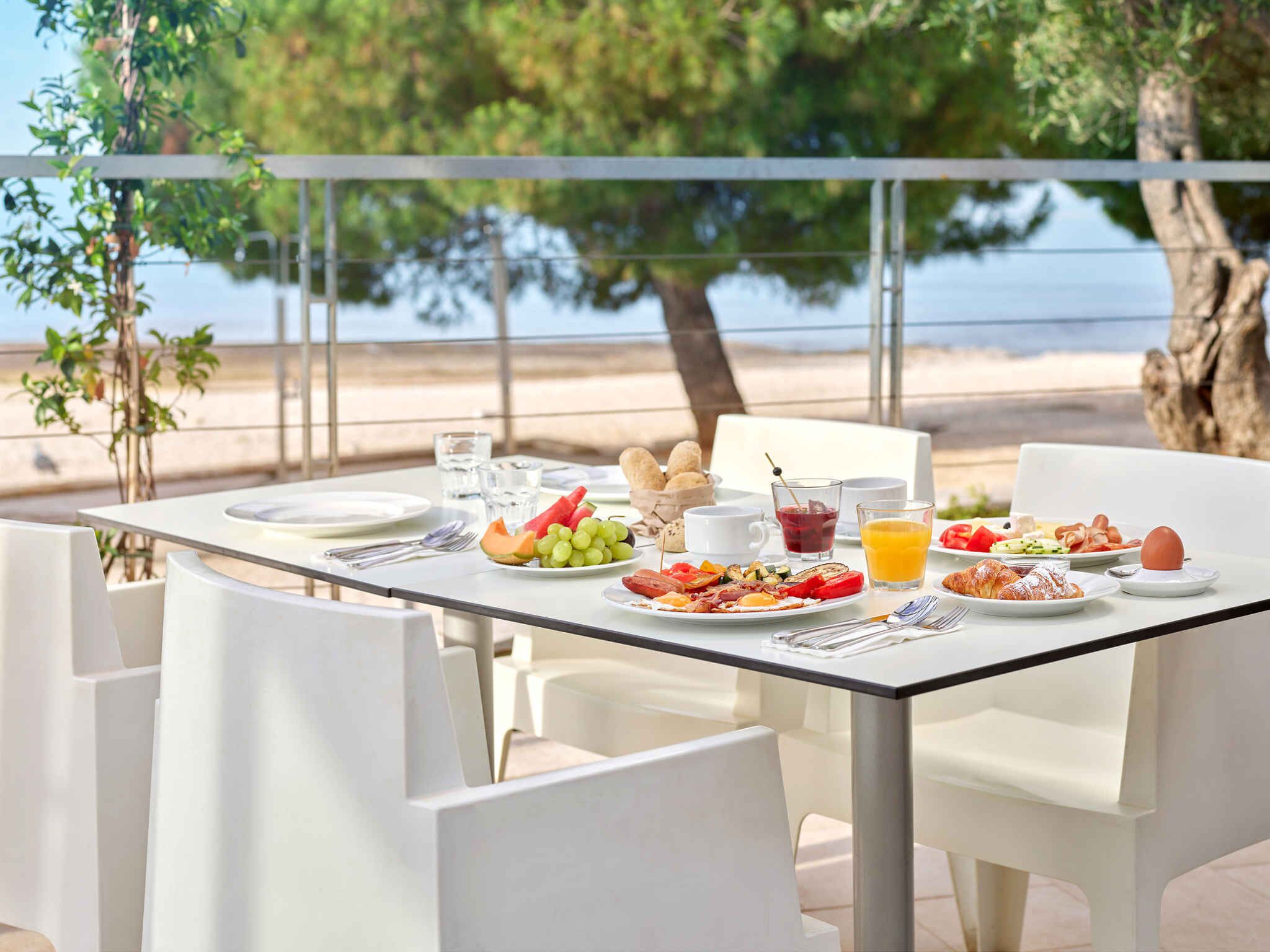 Una tavola imbandita con piatti di cibo, bicchieri di succo e vista sulla spiaggia.