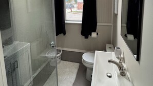 A bathroom with a shower, toilet, sink, and a window with curtains. - Riverside apartment in Bay City perfect for your next getaway (Bay City)