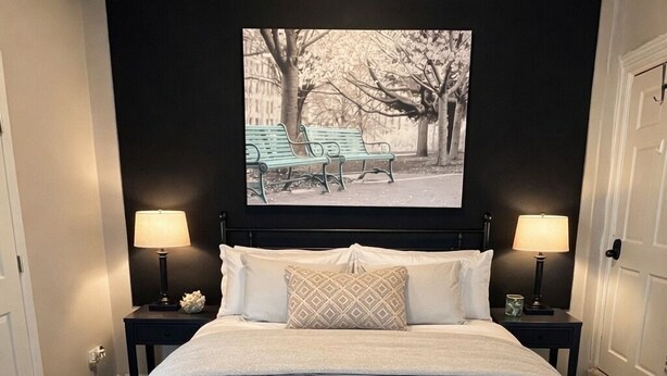 A bedroom with a bed, two bedside tables, a bench, a wall-mounted picture, and a door. - Riverside apartment in Bay City perfect for your next getaway (Bay City)
