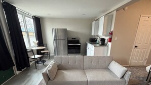 A compact living space with a sofa, dining table, chairs, a kitchenette, and a window with curtains. - Riverside apartment in Bay City perfect for your next getaway (Bay City)