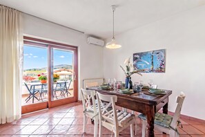 Un coin repas avec une table dressée pour quatre personnes, une grande fenêtre donnant sur l’extérieur et un appareil de climatisation fixé au plafond.