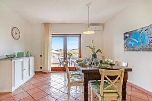 Un área de comedor con vistas al exterior, una mesa de comedor dispuesta con platos y vasos, un reloj en la pared y un cuadro en la pared.