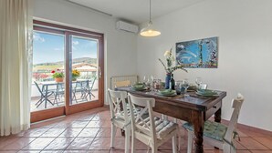 A dining area with a table set for four, white chairs, a painting on the wall, and a view through the glass door. - Villa Adriana Capalbio With A/c, BBQ and Parking (Capalbio)