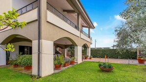 A two-story building with a covered patio area, potted plants, and a well-maintained lawn. - Villa Adriana Capalbio With A/c, BBQ and Parking (Capalbio)