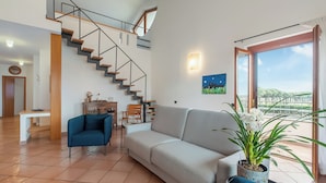 A spacious living area with a staircase, a sofa, a dining table, and a potted plant. - Villa Adriana Capalbio With A/c, BBQ and Parking (Capalbio)