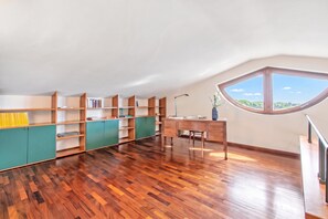 Une pièce spacieuse dotée d’un plancher en bois, d’un bureau, d’une chaise et d’une grande fenêtre donnant sur un paysage verdoyant.