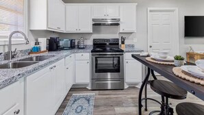 A modern kitchen with white cabinets, stainless steel appliances, a granite countertop, and a bar stool.