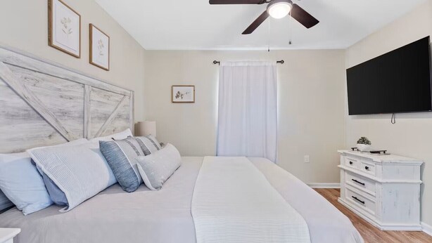 A bedroom with a large bed, a ceiling fan, a TV, and a dresser.