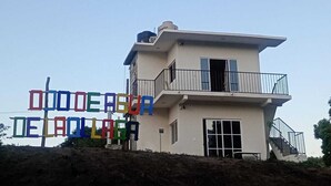 A two-story building with a balcony on the upper floor, a large window on the lower floor, and a sign with colorful letters. - Hospedaje ojo de agua (Santiago Laollaga)