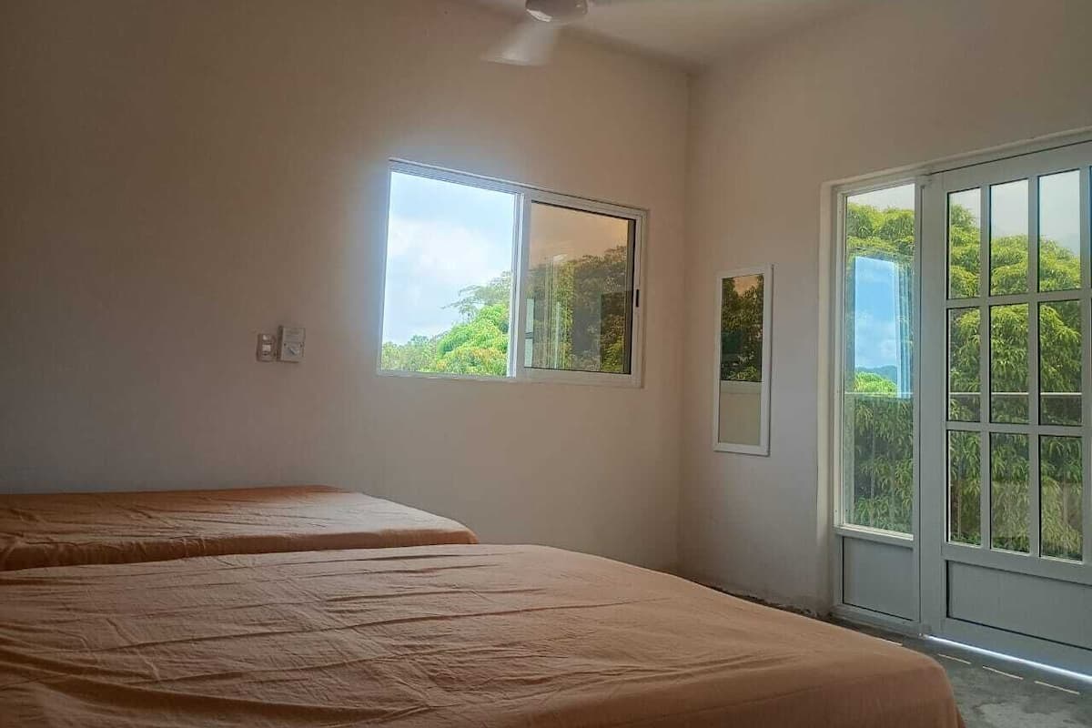 A room with two beds, a ceiling fan, a window, and a door leading outside.