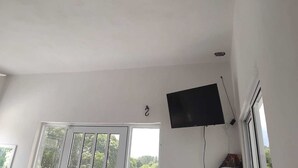A room with a large window, a flat-screen TV mounted on the wall, and a ceiling light. - Hospedaje ojo de agua (Santiago Laollaga)
