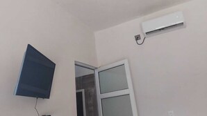 A room with a flat-screen TV mounted on the wall, an air conditioning unit, and a window with a view. - Hospedaje ojo de agua (Santiago Laollaga)