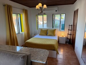 Ein Schlafzimmer mit Bett, Nachttisch, Lampe, Fenster mit Vorhängen und Holzboden.