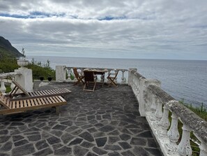 Una terrazza con pavimento in pietra, un tavolo con sedie e vista sul mare.