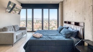 A modern bedroom with a large bed, a sofa, and a city view through large windows. - Casa Grace a pasos de Polanco y Reforma. (Ciudad de México)