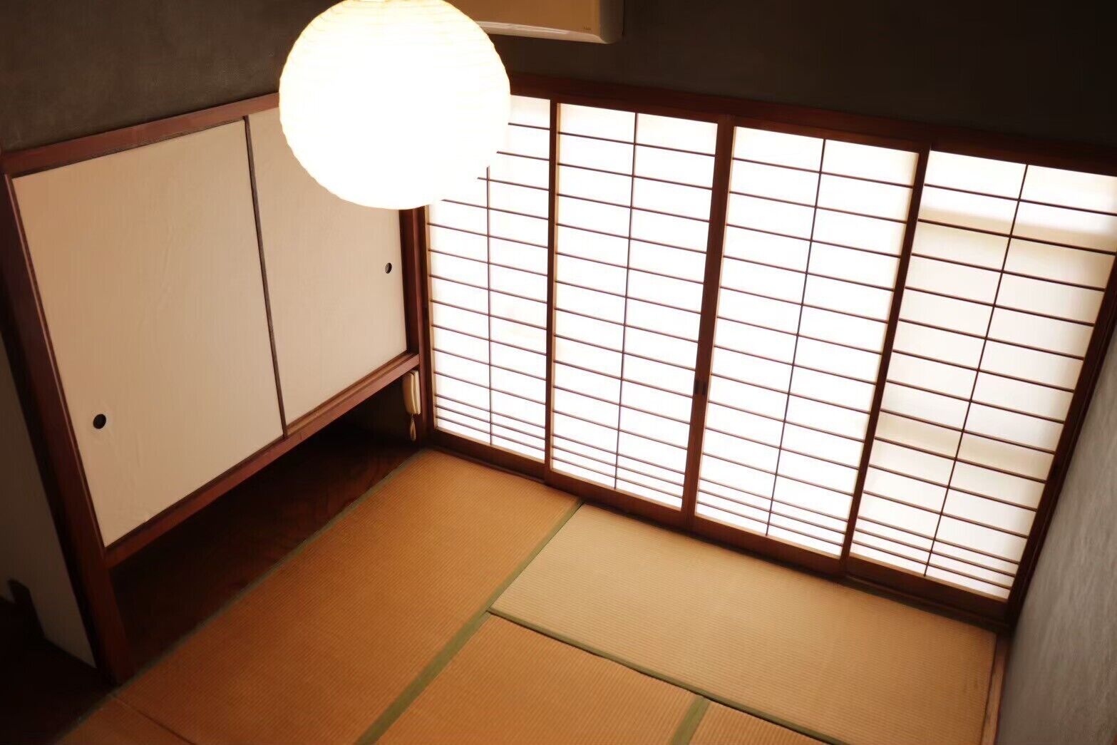 Una habitación japonesa tradicional con suelo de tatami, puertas correderas y una lámpara colgante.