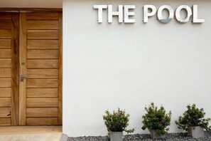 Eine Holztür, ein Schild mit der Aufschrift 'THE POOL' und drei Kübelpflanzen.