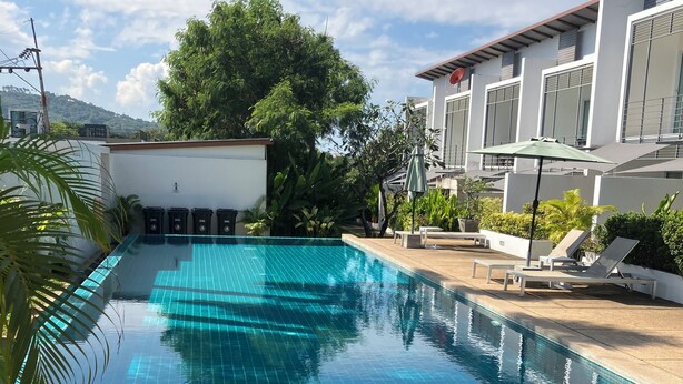 Una piscina con suelo de baldosas, rodeada de sillones de descanso y plantas en macetas.