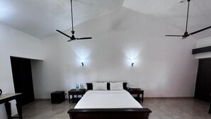 Une chambre à coucher avec un grand lit, deux tables de chevet, une commode, un ventilateur de plafond et un luminaire fixé au mur.