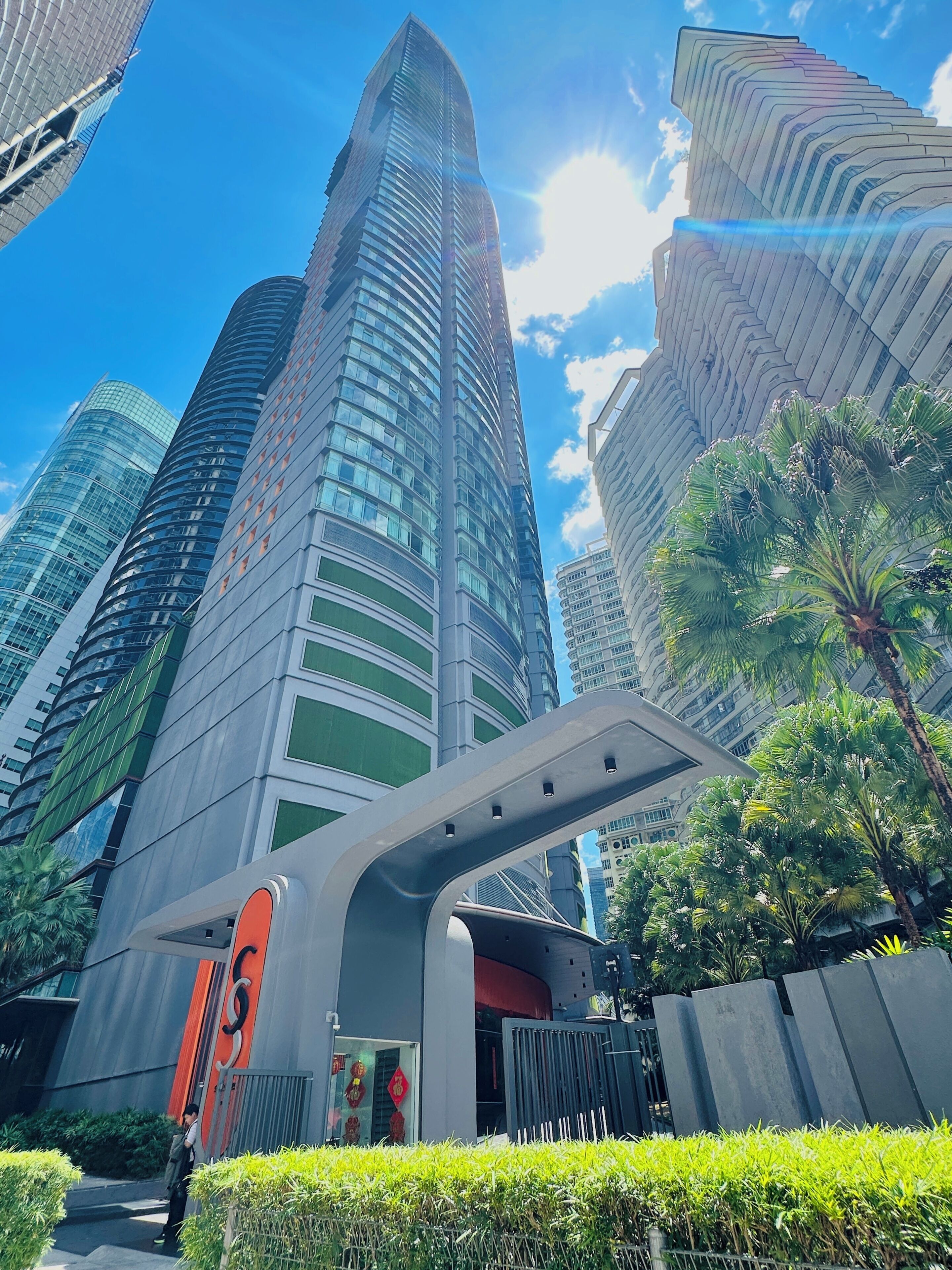A modern high-rise building with a curved facade, surrounded by other tall structures and greenery.
