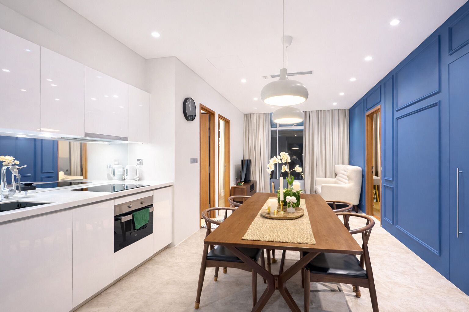 Een moderne keuken met witte kastjes, een houten eettafel en een blauwe accentmuur.