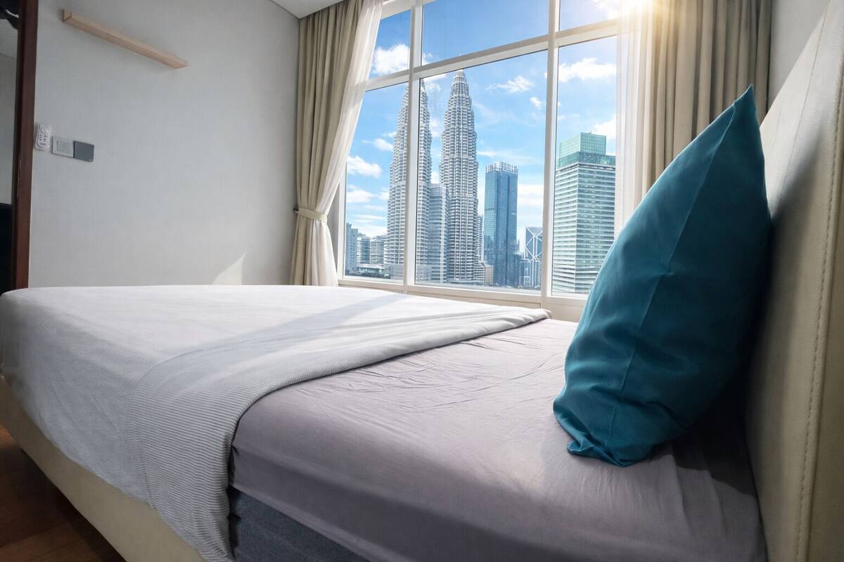 A hotel room with a bed, a window with a cityscape view, and a wooden shelf.