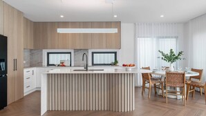Eine moderne Küche mit Kochinsel, Holzschränken und einem Essbereich mit rundem Tisch und Stühlen.