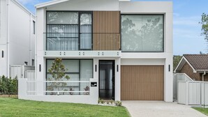 Ein modernes, zweistöckiges Haus mit weißer Fassade, großen Fenstern und einer Holztür zur Garage.