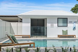 A modern building with a pool, two lounge chairs, and a bench. - Beachside on Beecroft (Huskisson)