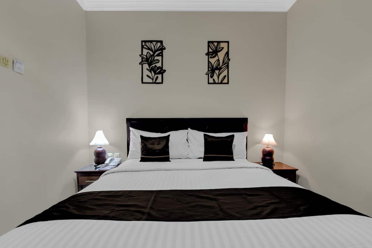Ein ordentlich bezogenes Bett mit weißer und schwarzer Bettwäsche, zwei Nachttischlampen und zwei an der Wand befestigte Blumendekorationen.