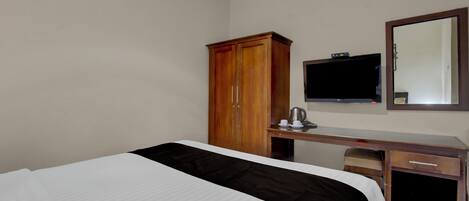 A hotel room with a bed, a wooden wardrobe, a desk with a television, and a mirror.