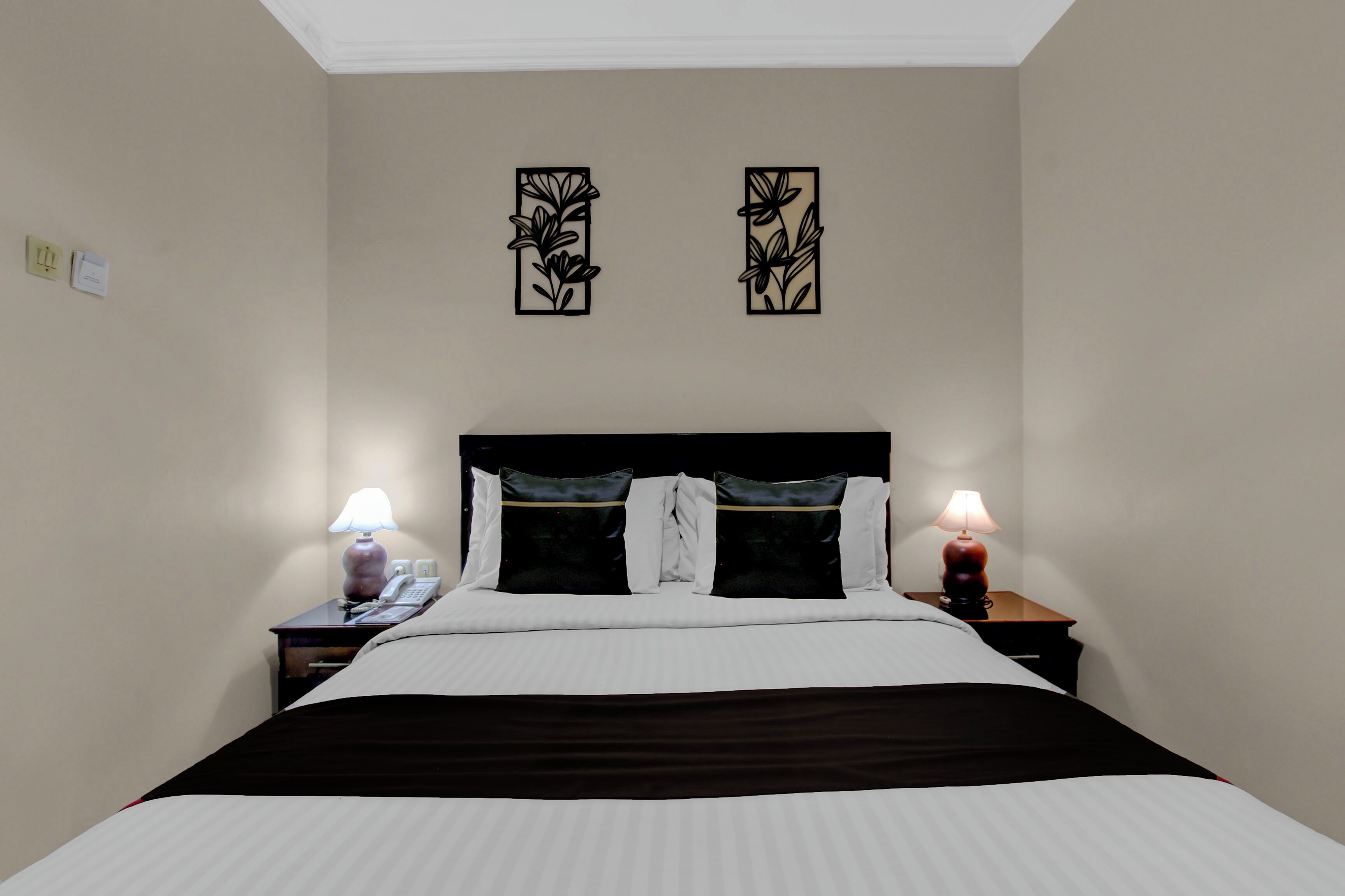 Une chambre à coucher comprenant un lit, deux tables de chevet, des lampes et deux décorations florales fixées au mur.