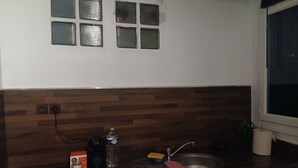 Cuina amb salabost a la paret de fusta, una finestra amb persianes, un rentapeus i diversos objectes de cuina.