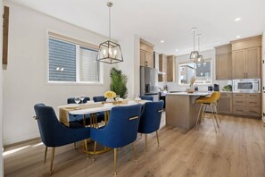 A modern kitchen with wooden cabinets, a central island, and a dining area with blue chairs. - Charming 3-bedroom house in beautiful Calgary with AC (Calgary)