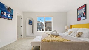 Un dormitorio moderno con una cama grande, una ventana con vistas a edificios, una puerta y una pared decorada con un póster.