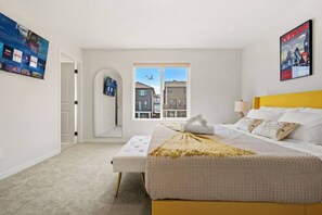 A modern bedroom with a large bed, a window with a view of buildings, a door, and a wall with a poster. - Charming 3-bedroom house in beautiful Calgary with AC (Calgary)