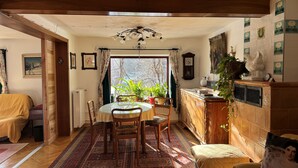 Een eetgedeelte met een ronde tafel, stoelen, een radiator, een klok en een raam met gordijnen.