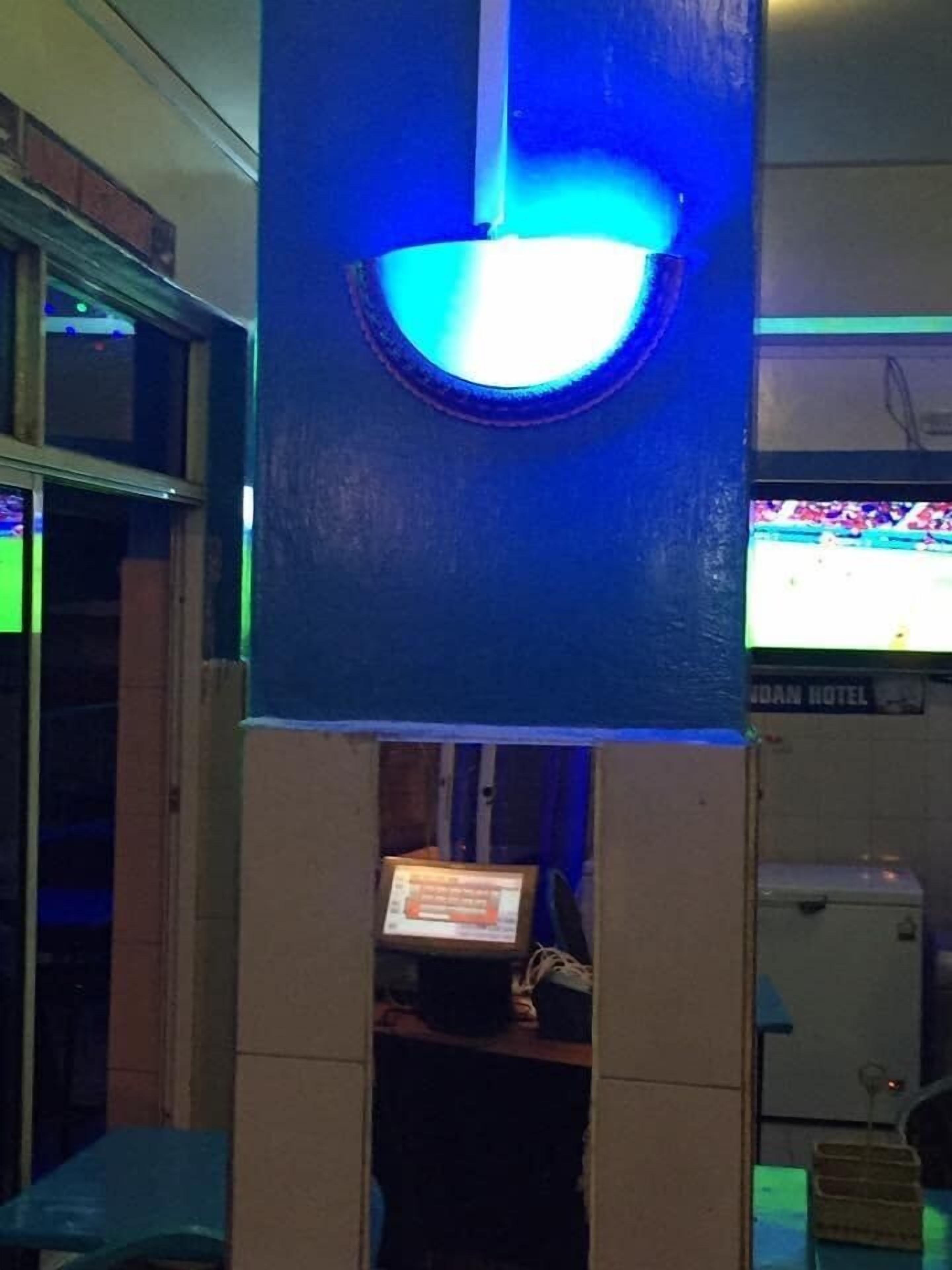 Ett rum med en blå vägg, en blå lampa som är tänd, en tv-skärm och en skylt med texten ”INDIAN HOTEL”.