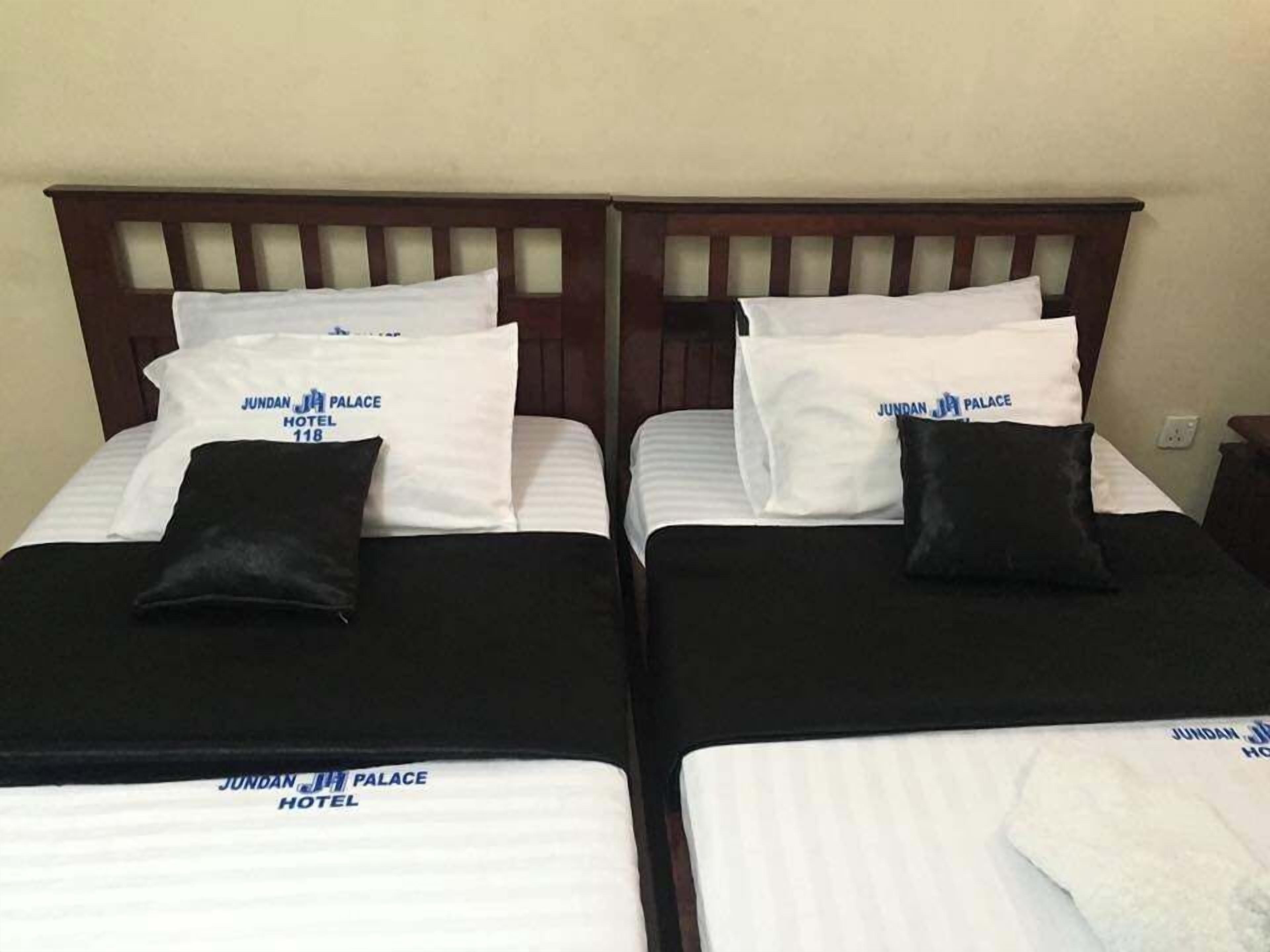 Dos camas individuales con sábanas blancas y cabeceros negros, cada una con una almohada que dice 'JUNDAN JI PALACE HOTEL'.