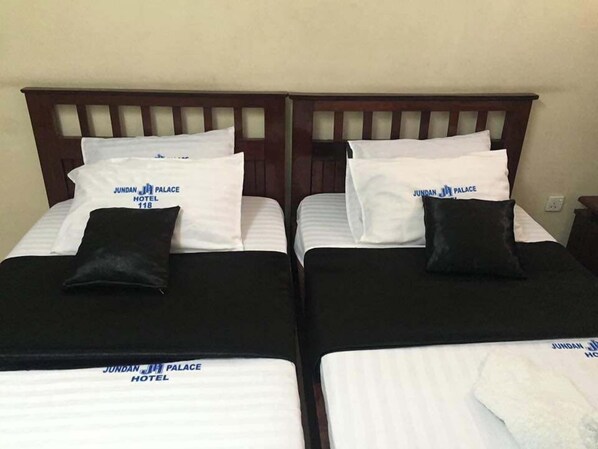 Two twin beds with white linens and black headboards, each with a pillow labeled 'JUNDAN JI PALACE HOTEL.' - Jundan Palace Hotel Mombasa (Mombasa)