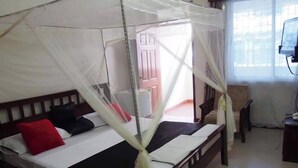 A bed with a mosquito net, a wooden headboard, and a red pillow. - Jundan Palace Hotel Mombasa (Mombasa)