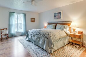 Une chambre à coucher comprenant un lit, une table de chevet, une chaise, une fenêtre avec des rideaux et un ventilateur de plafond.