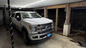 En vit SUV står parkerad i ett svagt upplyst garage med ett betonggolv och en vägg som är delvis under uppförande.