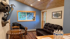 A wooden ceiling, a dining area with chairs, a wooden table, a leather couch, a window with a view, and mounted bird figures.