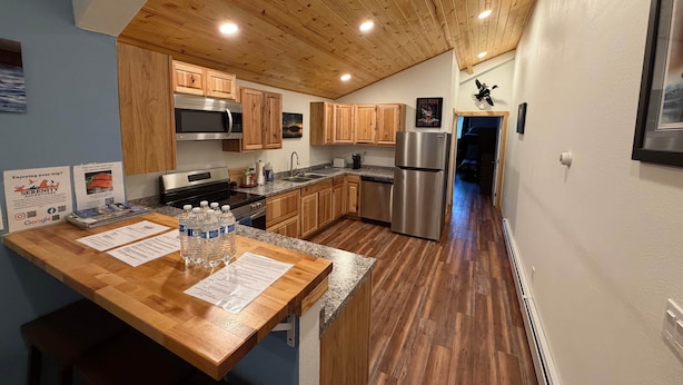 A modern kitchen with wooden cabinets, stainless steel appliances, and a wooden ceiling.