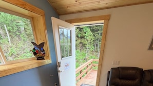 A room with a wooden floor, a black leather sofa, a dog, a door leading outside, and a window with a bird decoration.