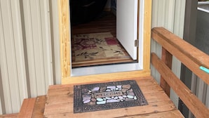 A wooden door leading to a room with a window, a welcome mat, and a doorbell.