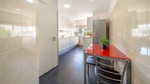 A modern kitchen with a red table and chairs, a refrigerator, and cabinets. - GuestReady - Retreat in Almada (Almada)