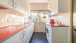 A compact kitchen with a washing machine, a window, and a red countertop. - GuestReady - Retreat in Almada (Almada)