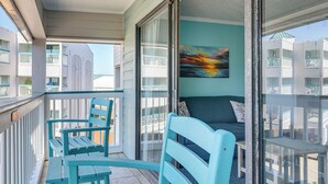 Un balcon avec une porte vitrée, un fauteuil turquoise, un canapé et un tableau accroché au mur.